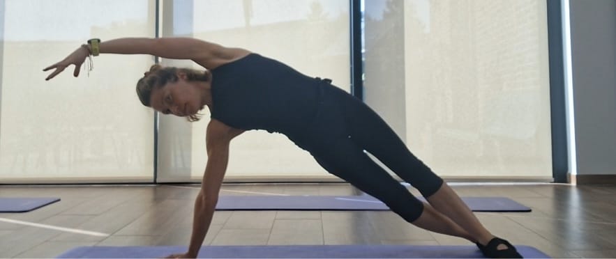 Ludivine en planche latérale sur un tapis, un bras tendu au-dessus de la tête, dans une salle lumineuse